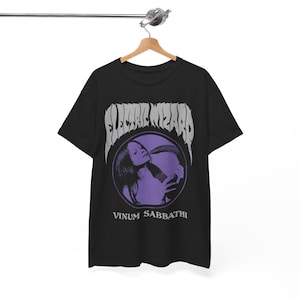 May include: Black t-shirt featuring a purple and white graphic. The graphic includes the band name "ELECTRIC WIZARD" above a circular image of a woman with a snake, and the words "VINUM SABBATHI" below.