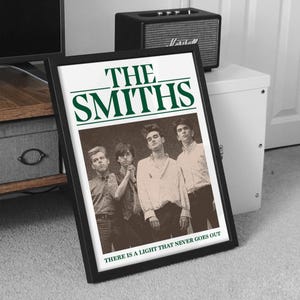 May include: A framed poster featuring the band The Smiths, with the band's name in green text at the top. The poster has a black frame and includes the text "THERE IS A LIGHT THAT NEVER GOES OUT" at the bottom.