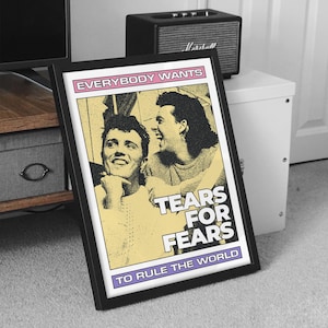 May include: Framed poster featuring the band Tears for Fears. The poster has a yellow background with the band members' faces and the text "EVERYBODY WANTS", "TEARS FOR FEARS", and "TO RULE THE WORLD". The frame is black.
