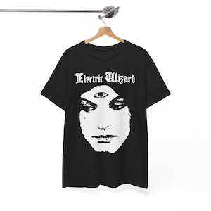 May include: Black t-shirt featuring a white graphic of a face with a third eye and the text "Electric Wizard" in a gothic font. The shirt is hanging on a wooden hanger.