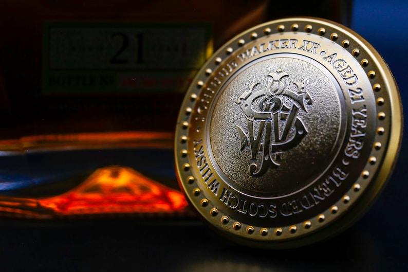 May include: A gold-colored metal cap with the words "Johnnie Walker Jr. Aged 21 Years - Blended Scotch Whisky" embossed around the edge. The center of the cap features a stylized "JW" logo.