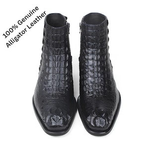 Könnte beinhalten: Ein Paar schwarze Stiefeletten mit texturiertem Alligatorhautmuster und seitlichem Reißverschluss. Der Text 100% Genuine Alligator Leather ist in der oberen linken Ecke aufgedruckt. Diese Stiefel haben eine eckige Zehenpartie und glänzende Optik.