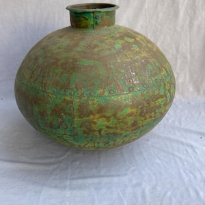 May include: A large, round metal vessel with a green and yellow patina. The vessel has a short, cylindrical neck and is riveted along the seams. The overall shape is bulbous, with a slightly flattened base. The metal has a weathered appearance.