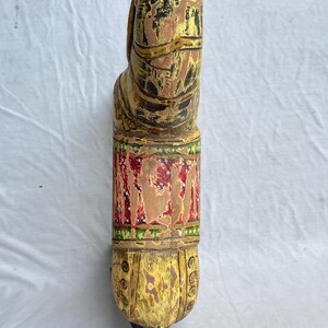 May include: A hand-carved wooden horse sculpture, painted in shades of yellow, brown, red, and green. The horse has detailed features and a decorative band around its midsection. The sculpture is a unique piece of home decor.
