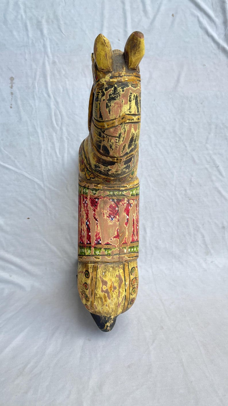 May include: A hand-carved wooden horse sculpture, painted in shades of yellow, brown, red, and green. The horse has detailed features and a decorative band around its midsection. The sculpture is a unique piece of home decor.