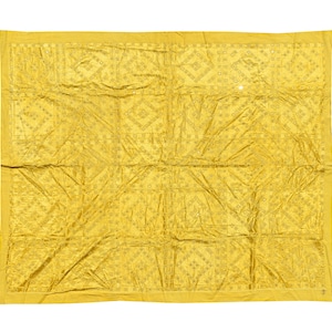 May include: A large, yellow textile with a repeating geometric pattern. The fabric has a slightly wrinkled appearance, and the design features squares and diamond shapes. The overall aesthetic is a blend of traditional and contemporary styles.