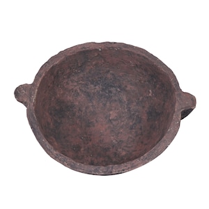 Può includere: Una ciotola rustica e rotonda color terracotta con interno scuro. La ciotola ha un bordo largo e due piccole maniglie arrotondate sui lati opposti. La superficie ha un aspetto strutturato.