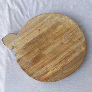 以下が含まれることがあります： ハンドル付きの丸い木製まな板。ボードは、木目がはっきりと見える明るい茶色の木材で作られています。ハンドルは、ボードの側面から伸びる小さな長方形の形をしています。このボードは、食品の準備に使用される可能性があり、直径は約25cmです。