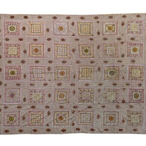 May include: A rectangular, off-white textile with a repeating pattern of squares and decorative elements. The squares contain various designs in shades of yellow, pink, and brown. The textile is likely a quilt or decorative fabric.