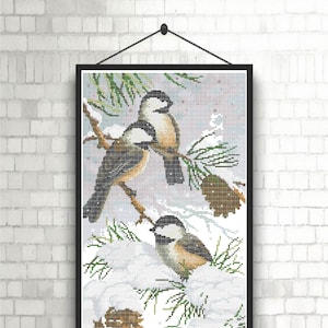 Könnte beinhalten: Zwei braune und weiße Vögel sitzen auf einem schneebedeckten Ast mit Kiefernnadeln und Zapfen. Die Vögel haben schwarze Augen und Schnäbel. Der Hintergrund ist ein verschwommenes Weiß und Blau.