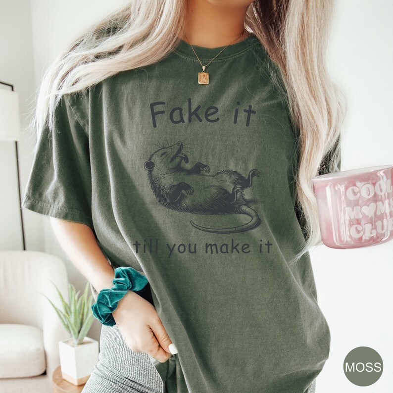 May include: A green t-shirt with a black graphic of a possum and the text "Fake it till you make it".