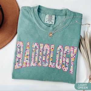 May include: Light green t-shirt with a floral print design that spells out the word "RADIOLOGY".