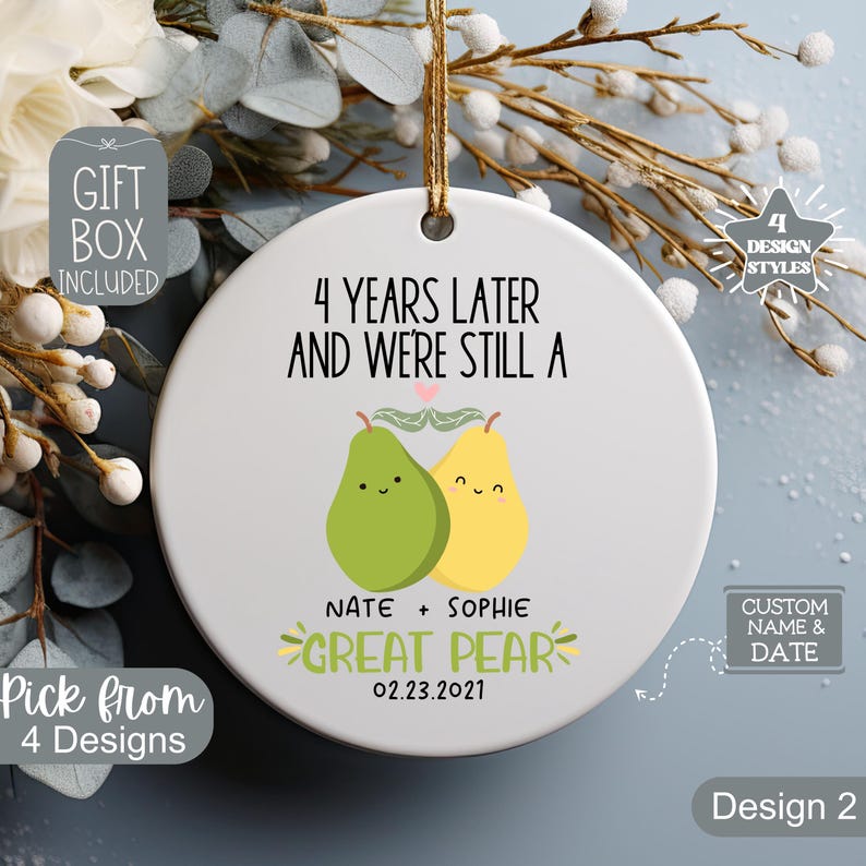 May include: A white ceramic ornament with the text "4 YEARS LATER AND WE'RE STILL A" and "GREAT PEAR". It features two cartoon pears, one green and one yellow, with the names "Nate + Sophie" and the date "02.23.2021".