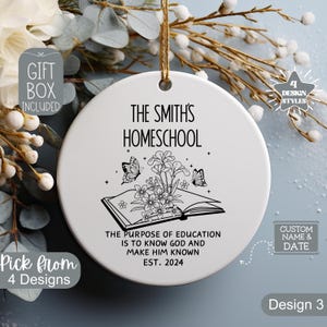 K&ouml;nnte beinhalten: Wei&szlig;er Keramik-Anh&auml;nger mit schwarzem Text und einer Schwarzwei&szlig;-Illustration eines Buches mit Blumen und Schmetterlingen. Der Text lautet "The Smith's Homeschool The purpose of education is to know God and make him known Est. 2024"