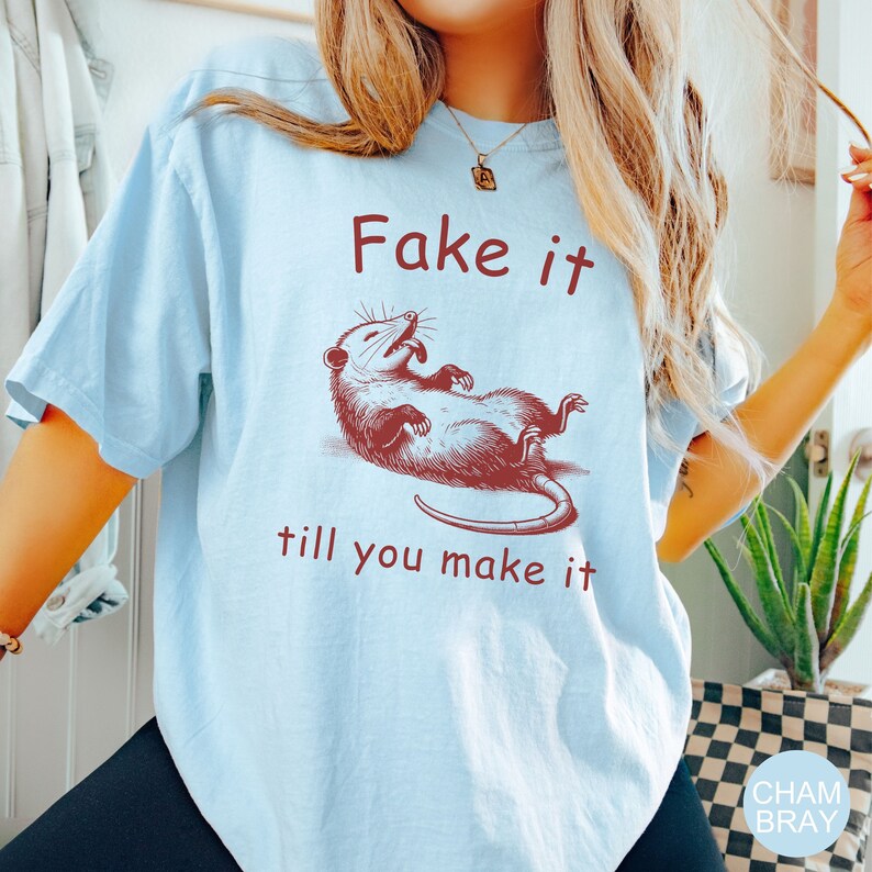May include: A light blue t-shirt with a red graphic of a possum with the text "Fake it till you make it".