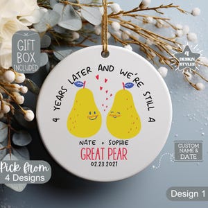 May include: A white ceramic ornament with a gold string for hanging. The ornament features two yellow pear illustrations with the text "4 years later and we're still a great pear." Includes names and a date.