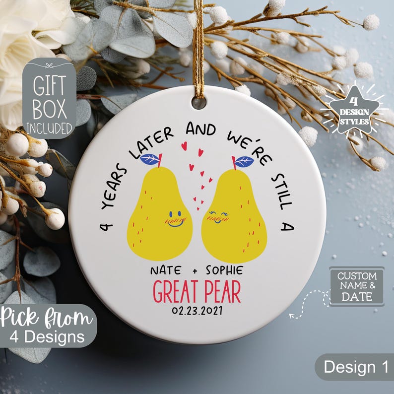 May include: A white ceramic ornament with a gold string for hanging. The ornament features two yellow pear illustrations with the text "4 years later and we're still a great pear." Includes names and a date.