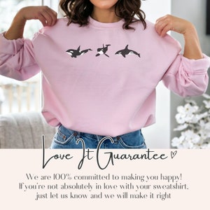 May include: Pink sweatshirt featuring a graphic of three black and white orcas. The text "Love It Guarantee" is written below the image.