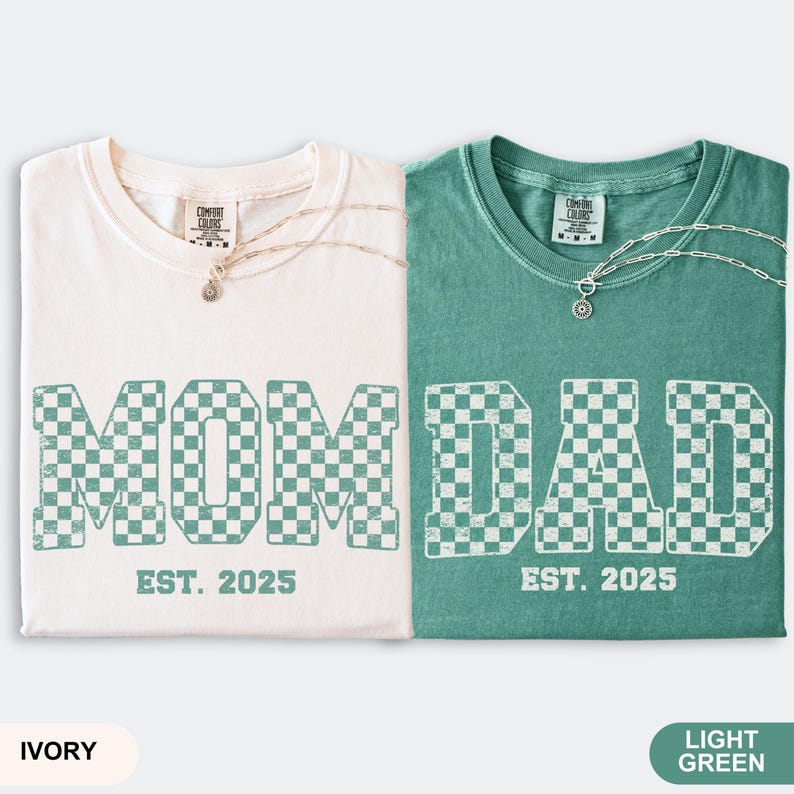 May include: Two t-shirts, one ivory and one light green, with the words "MOM" and "DAD" in a checkered pattern. The text "EST. 2025" is below each word. Each shirt has a silver necklace. The bottom of the image has the color names.