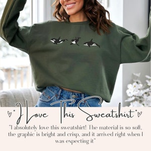 May include: A green sweatshirt featuring a graphic of three orcas swimming. The text "I love this sweatshirt" is written below the graphic.