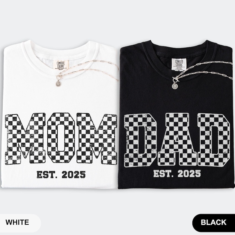 May include: Two t-shirts, one white and one black, with the words "MOM" and "DAD" in a checkered pattern. The text "EST. 2025" is below each word. Each shirt has a silver necklace. The white shirt is labeled "WHITE" and the black shirt is labeled "BLACK".