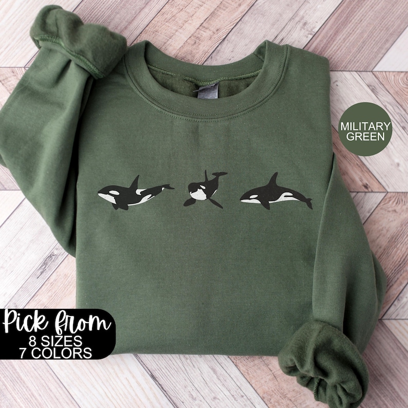 May include: A green sweatshirt with a graphic of three orcas in a row. The text "Pick from 8 sizes 7 colors" and "Military Green" are on the sweatshirt.