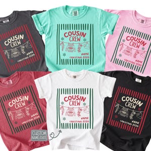 Könnte beinhalten: Sechs kurzärmelige T-Shirts in Anthrazit, Mint, Rosa, Rot, Weiß und Schwarz. Jedes zeigt den Text COUSIN CREW, NAME und CHRISTMAS 2026 sowie Illustrationen von Zuckerstange, Pullover, Socke und Mütze als grafisches Motiv.
