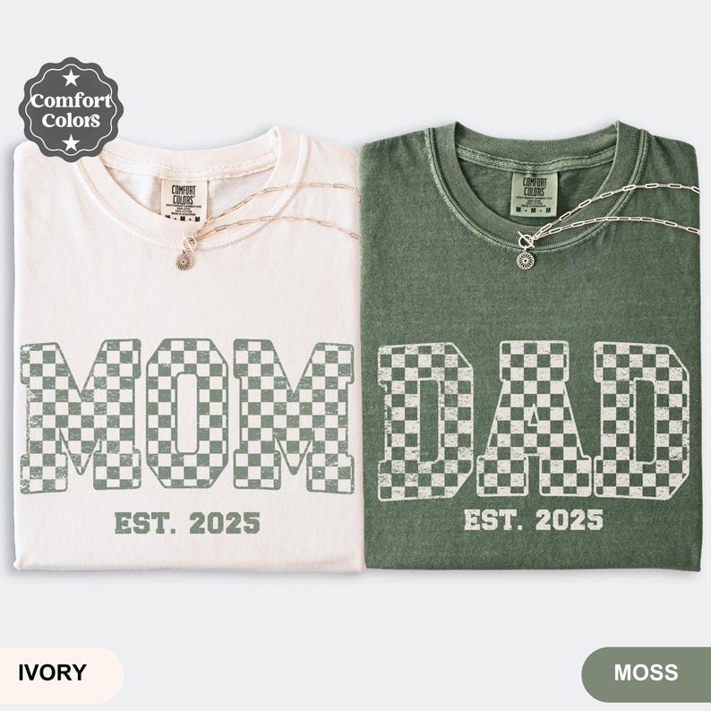 May include: Two Comfort Colors t-shirts, one ivory and one moss green, with the words "MOM" and "DAD" in a checkered pattern. Each shirt has "EST. 2025" printed below the text. The ivory shirt has a silver necklace.