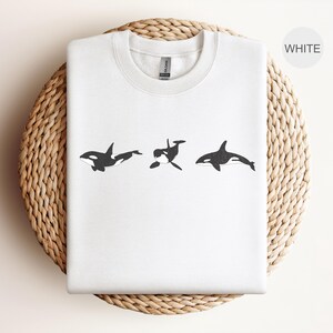 May include: White sweatshirt with a graphic of three black and white orcas swimming in a row.