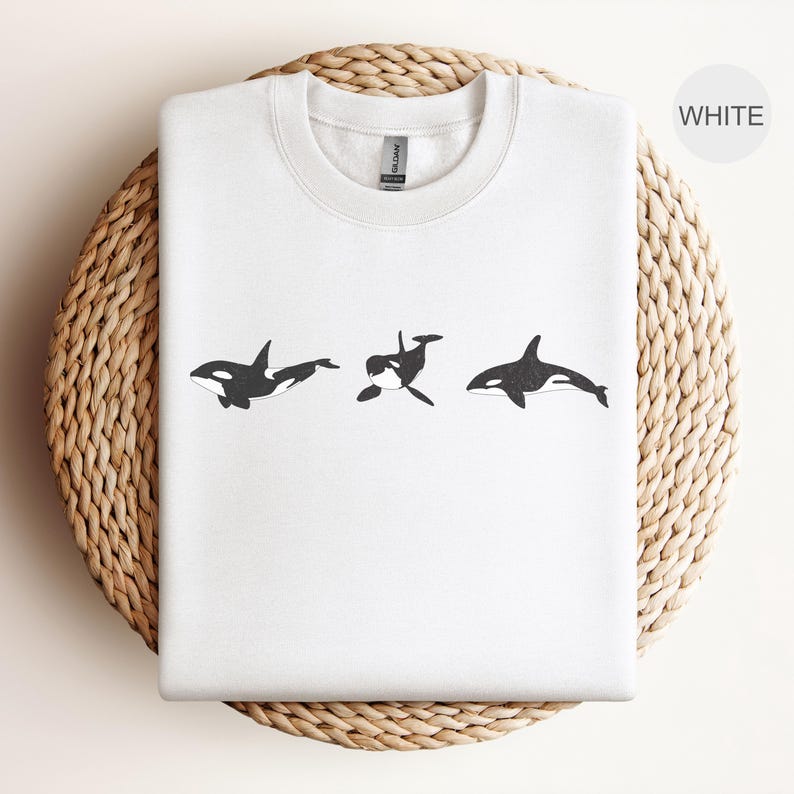 May include: White sweatshirt with a graphic of three black and white orcas swimming in a row.