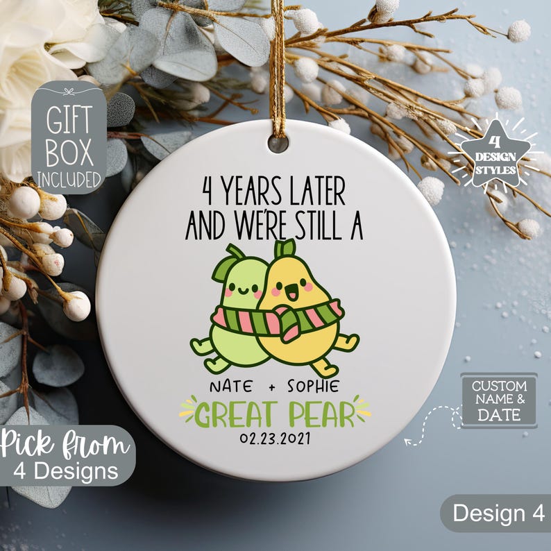 May include: White ceramic ornament with the text "4 Years Later And We're Still A Great Pear" and a cartoon pear couple. Includes the names "Nate + Sophie" and the date "02.23.2021". Features a gold string for hanging.
