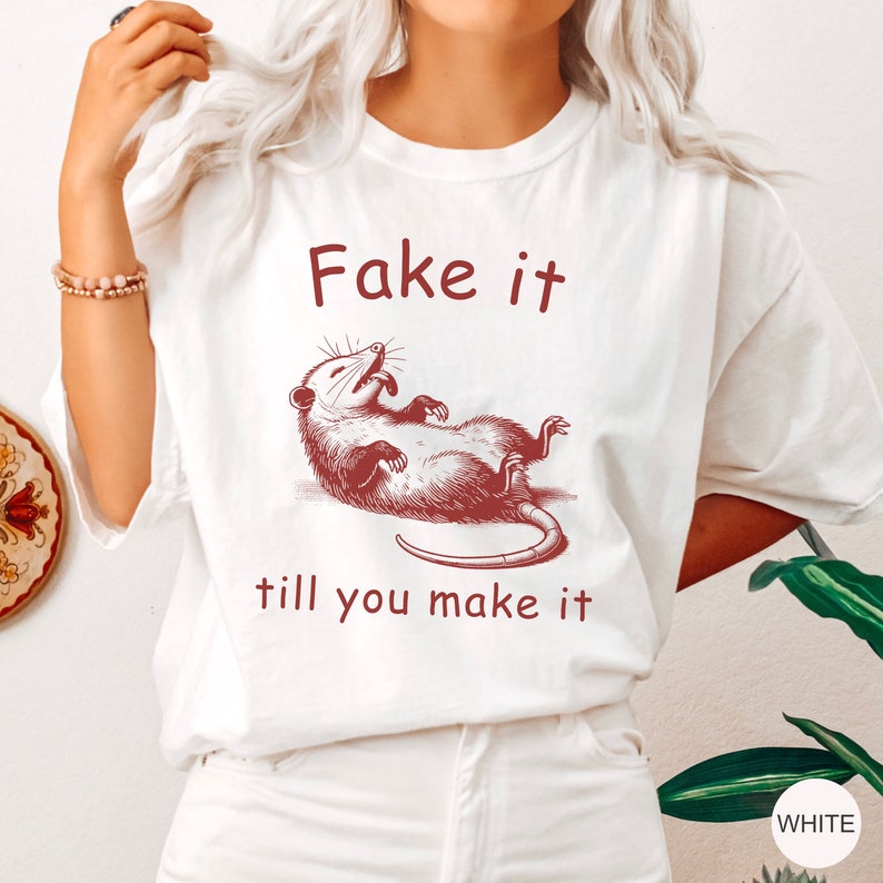 May include: White t-shirt with a red graphic of a possum and the text "Fake it till you make it".