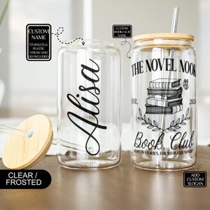 K&ouml;nnte beinhalten: Zwei klare Glasbecher mit Deckel und Strohhalmen. Ein Becher hat den Namen "Alisa" darauf geschrieben. Der andere Becher hat den Text "The Novel Nook Book Club Est. 2024 Lost in stories, found in friendship".