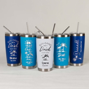 May include: Five stainless steel tumblers with various designs and text. The tumblers are blue, white, and silver. The text on the tumblers includes "Sun and a Drink", "Hello Girl's Trip", "Donti Key West 2021", "Blaine Dubai 2023", and "Laura Dubai 2023".