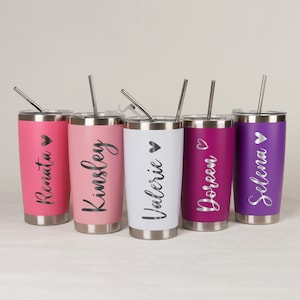 May include: Five stainless steel tumblers with personalized names and a heart symbol. The tumblers are in various colors: pink, white, purple, and a darker shade of purple. Each tumbler has a straw.