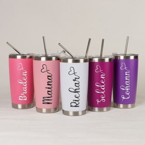 May include: Five stainless steel tumblers with personalized names and a heart design. The tumblers are in various colors, including pink, white, and purple. Each tumbler has a matching straw.