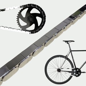 Puede incluir: Una cadena de bicicleta con un pi&ntilde;&oacute;n negro y una cadena negra y plateada. Una bicicleta negra est&aacute; en el fondo. La cadena est&aacute; hecha de eslabones rectangulares de color plateado.