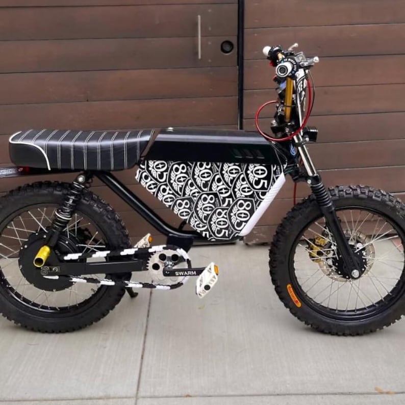 May include: Black and white electric bicycle with a patterned design on the side panel. The bike has a black frame, seat, and tires. The wheels have a black and white pattern. The text "SWARM" is visible on the pedals.