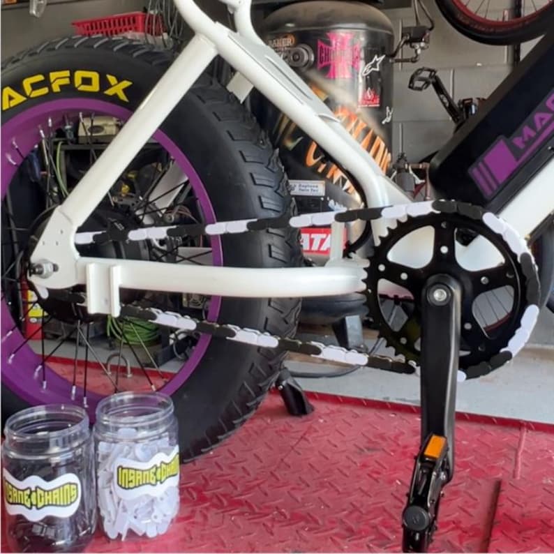 May include: White and purple fat tire bicycle with black tires and a black and white chain guard. The bicycle has the text "ACFOX" on the tire. Two jars of chain accessories are in front of the bike.