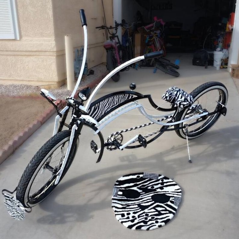 May include: A custom bicycle with a white frame, black tires, and zebra print accents on the seat, fenders, and footrests. A matching zebra print rug is in front of the bike. The bike has a unique curved design.