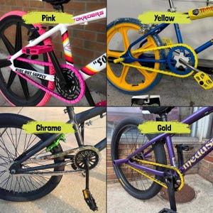 May include: Four BMX bikes with different color schemes. One bike has pink accents, another has yellow, a third has chrome, and the last one has gold. Each bike has a unique design and color combination.