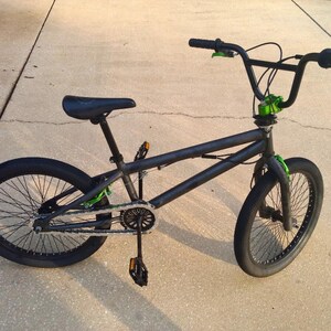 Puede incluir: Una bicicleta BMX negra con detalles verdes en el manillar, la horquilla y la cadena. La bicicleta tiene neum&aacute;ticos negros, un asiento negro y un cuadro negro. La bicicleta est&aacute; dise&ntilde;ada para acrobacias y trucos.
