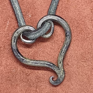 May include: A silver heart-shaped pendant necklace with a leather cord. The pendant is made of metal and has a textured surface.