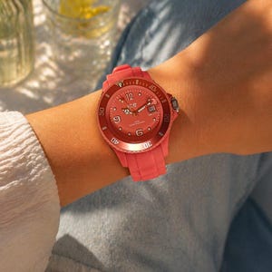 May include: A coral-colored wristwatch with a round face and a matching silicone band. The watch face displays the number 12, the brand name "Ice", and the date. The watch is water resistant.