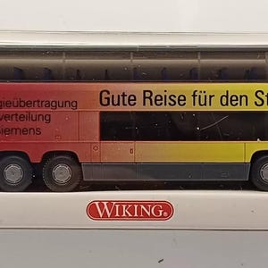 Könnte beinhalten: Ein Modellbus in einer transparenten Kunststoffbox. Der Bus ist rot, orange und gelb mit dem Text "Energieübertragung und -verteilung von Siemens" und "Gute Reise für den Strom". Das Modell befindet sich in einer weißen Box mit dem "WIKING"-Logo.
