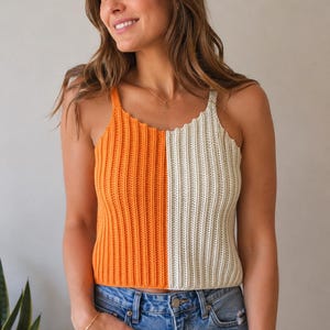 May include: A sleeveless crochet tank top featuring a vertical split-color design with one half in bright orange and the other half in off-white. The garment has a ribbed texture, a scoop neckline, and thin shoulder straps, paired with blue denim jeans.