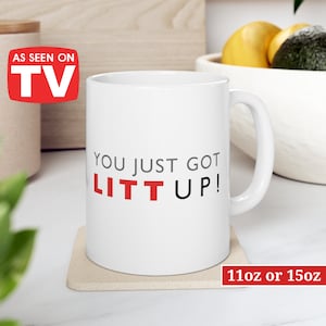 May include: White ceramic mug with a black and red design that says "You just got LIT UP!"  The mug is sitting on a beige coaster. The mug is available in 11 oz or 15 oz sizes.