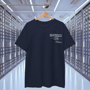 Może przedstawiać: Koszulka w kolorze granatowym z białym nadrukiem graficznym z napisem "Macrodata Refinement - Lumen - Debbie B."