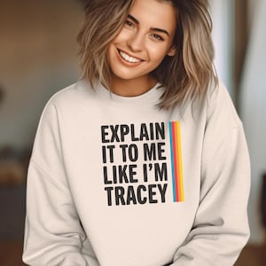 Op de afbeelding: Een wit sweatshirt met de tekst "Explain it to me like I'm Tracey" in zwarte letters met een regenboogstreep aan de rechterkant.