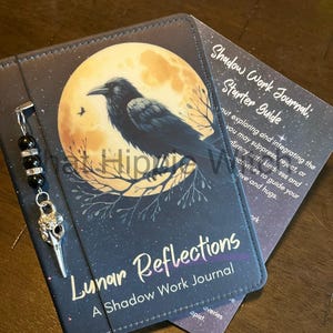 May include: A black leather journal with a moon and raven design. The journal is titled "Lunar Reflections: A Shadow Work Journal".
